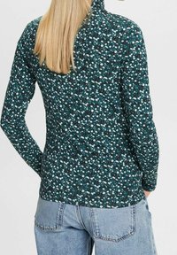 Maglietta a maniche lunghe in verde scuro con un motivo floreale. Tessuto morbido con un design aderente, orlo arrotondato e una leggiera texture.