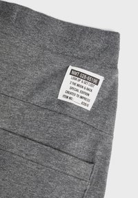 Grå bomulls joggebukser med ribbet midjebånd og et merke med tekst. Designet inkluderer to sidelommer og en myk tekstur.