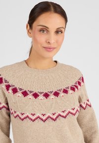 Suéter de punto beige que cuenta con un escote redondo, patrón texturizado y acentos geométricos coloridos en tonos de carmesí y crema alrededor de la sisa.
