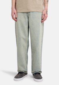 Μπλε ξεβαμμένο τζιν με χαλαρή εφαρμογή, ίσια μπατζάκια και διακριτικές λεπτομέρειες υφής, συνδυασμένο με γκρι αθλητικά παπούτσια.