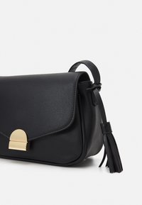 Czarna skórzana torebka o eleganckim designie, z ozdobą z złotego metalu i frędzlem. Płaskie zamknięcie i boczny pasek ułatwiają noszenie.