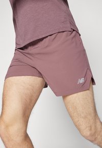 Vieglie sporta šorti mauve krāsā ar smalku rakstainu tekstūru. Ir sānu griezums un atstarojošs pelēks logotips apakšējā malā.