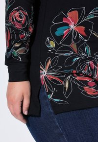 Czarny top z długim rękawem z kolorowymi kwiatowymi wzorami w kolorach czerwonym, różowym i niebieskim. Boczne rozcięcia i luźny krój, zestawiony z ciemnoniebieskimi dżinsami.