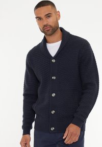 Cárdigan de punto en color navy con un patrón texturizado, cuello de chal y cierre de cinco botones con botones en contraste.