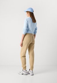 Ljusblå långärmad skjorta, beige joggare med elastisk midja och vita sneakers med svarta accenter, sedd bakifrån.