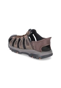 Brown athletic sandals with a mesh upper, multiple cutouts, and an adjustable lace system. Features a textured rubber sole with orange accents.