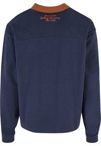 Marineblå langermet polo skjorte med en oransje ribbestrikket krage, prydet med brodert merke på baksiden og en jevn, bomullslignende tekstur.