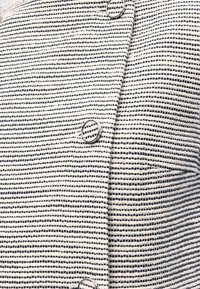 Ύφασμα με λευκές και ναυτικό μπλε ρίγες με υφαντή υφή, που διαθέτει ραφή και τρία ασημένια κουμπιά σε σχήμα δακτυλίου σε μια κάθετη σειρά.