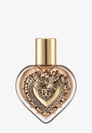 Flacon de parfum en forme de cœur avec un emblème décoratif doré présentant un nœud et les initiales "DG", coiffé d’un bouchon doré lisse.
