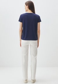 Camicetta blu navy a maniche corte con scollatura tonda, tessuto morbido e vestibilità comoda, abbinata a pantaloni bianchi e scarpe di colore chiaro.