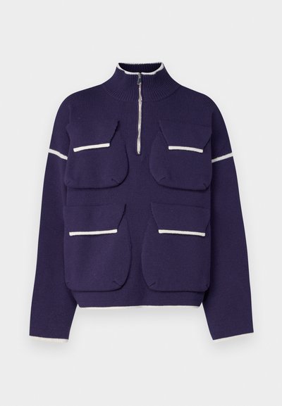 Lilla kootud pullover, millel on kõrge krae, pool tõmblukk ja neli esist kotti valge äärega. Sujuv tekstuur ja struktureeritud disain.
