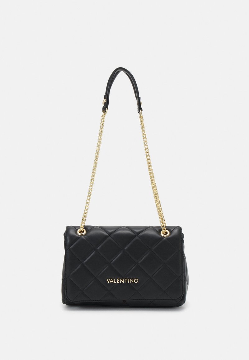 Zwarte gewatteerde handtas met een gouden kettinghengsel, met een gladde textuur en een logo aan de voorkant. Compakte rechthoekige vorm.