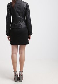 Svart läderjacka med en figursydd silhuett, kombinerad med en svart klänning och silvriga remsandaler med hög klack. Slät textur.