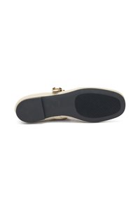 Zapato beige claro con parte superior de cuero liso, punta redonda y suela de goma negra con un patrón texturizado. Detalle de acento en hebilla dorada.