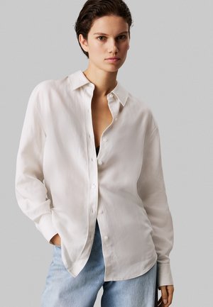 Hvid skjorte med knapper lavet af glat stof, med krave, lange ærmer og en afslappet pasform. Sammen med blå denim jeans.