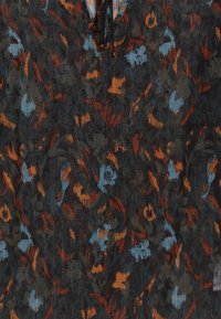 Tissu à motifs floraux dans des tons foncés avec des accents orange et bleu clair. Présente une surface texturée avec des détails visibles et un col à nouer.