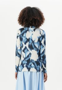 Langsleeve top in blauw en crème tie-dye patroon, met een ronde halslijn en een licht gebogen onderkant. Zachte stof met een gladde textuur.