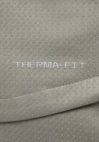 Primer plano de una tela gris con el logo "THERMA-FIT" bordado en hilo gris claro.