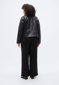 Μαύρο δερμάτινο μπουφάν με εφαρμοστή γραμμή, λεία υφή και κλείσιμο με φερμουάρ. Συνδυασμένο με μαύρο παντελόνι φαρδιάς γραμμής και παπούτσια με τακούνι block.