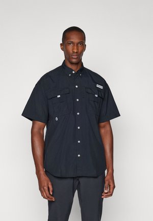 Camisa negra de manga corta hecha de material ligero, con dos bolsillos en el pecho, cierre de botones y una etiqueta en el lado izquierdo.