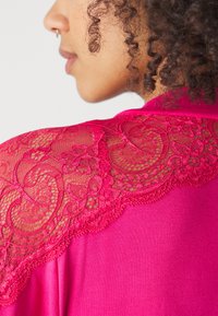 Haut fuchsia avec des détails en dentelle sur l'épaule ; présente des motifs floraux et des textures délicates, améliorant le design global avec un éclat doux.