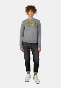 Maglione grigio a maglia con la scritta "EDIZIONE LIMITATA" in giallo. Jeans cropped blu navy con chiusura a due bottoni. Sneakers bianche con accenti colorati.