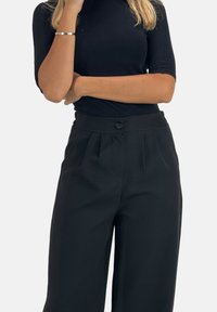Zwart nauwsluitend topje met korte mouwen en zwart high-waisted broek met knoopsluiting en geplooid voorpand. Soepele, lichtgewicht stof.