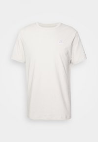 Ljusbeige bomullströja med rund halsringning, korta ärmar och en liten vit Nike-logotyp broderad på vänster bröst.