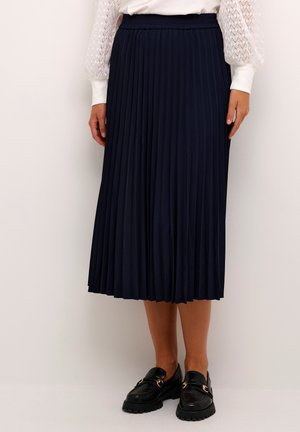 Marinblå plisserad midikjol i mjukt tyg med elastisk midja. Bärs med en vit långärmad skjorta och svarta loafers.