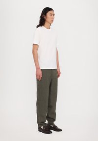 White short-sleeve t-shirt paired with olive-green, loose-fitting trousers and dark brown loafers featuring a gold accent. Minimalistic design.