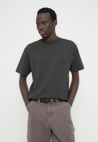 Σκοτό γκρι βαμβακερό μπλουζάκι με κοντά μανίκια και στρογγυλή λαιμόκοψη, συνδυασμένο με ανοιχτογκρι τζιν παντελόνι και μαύρη ζώνη με μεταλλικά διακοσμητικά στοιχεία.