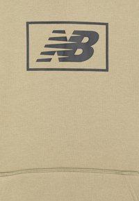 Světle béžová mikina s námořnickou modrou logem "NB" v obdélníkovém rámu. Hladký materiál s pečlivým prošíváním.