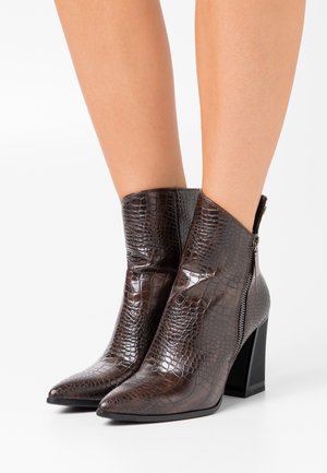 Bottes chevilles en croûte de crocodile marron avec un bout pointu et un talon carré. Équipées d'une fermeture éclair sur le côté pour un enfilage facile. Texture lisse.
