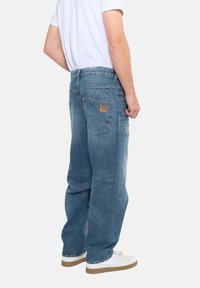 Jeans de denim azul claro con un corte relajado, que presentan una etiqueta de cuero en el bolsillo trasero y detalles de costura visibles.