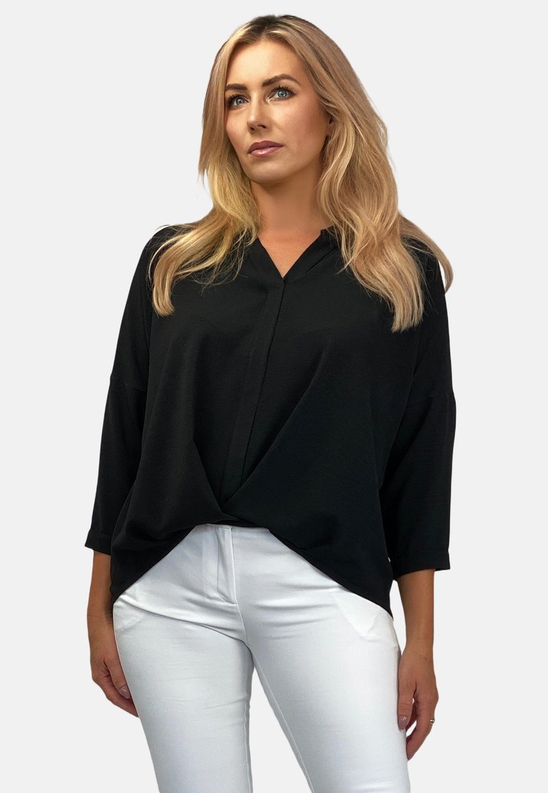 Czarna bluzka z dekoltem w serek i rękawami o długości trzech czwartych, wykonana z lekkiego materiału, luźno się układa, połączona z dopasowanymi białymi spodniami.