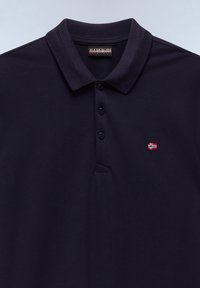 Polo azul marino con tres botones, cuello doblado, pequeño logo de la bandera noruega en el pecho y etiqueta de la marca en el interior del cuello.