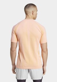 Camisa deportiva de color rosa claro con un patrón texturizado en la parte posterior, mangas cortas y un diseño de cuello redondo, acompañada de pantalones cortos grises.