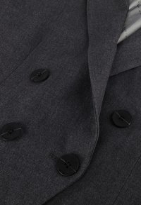 Grå dubbelknäppt blazer gjord av texturerat tyg som har svarta knappar och en slät innerfoder med ett subtilt mönster.