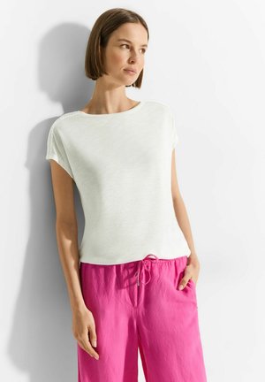 Top bianco a maniche corte con scollo rotondo e dettagli perforati sulle spalle, abbinato a pantaloni larghi fucsia con vita regolabile mediante cordino.