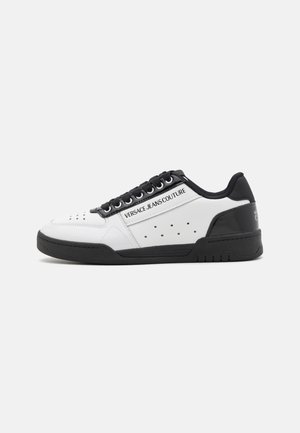 White leather sneaker with black accents, lace-up design, perforated detail on the sides, and branding on the side panel. Rubber sole.