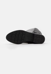 Bota negra de exterior con suela de goma texturizada, que presenta una parte superior de malla, puntera reforzada y un patrón de tracción detallado.