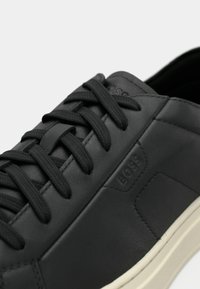 Czarny skórzany sneaker z teksturowanymi sznurowadłami, logo na boku oraz kontrastową białą podeszwą. Gładkie wykończenie w minimalistycznym stylu.