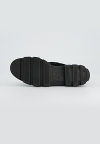 Semelle de sneaker noire présentant une surface texturée et rainurée avec des sections flexibles et un bout arrondi. Design minimaliste sans logos visibles.