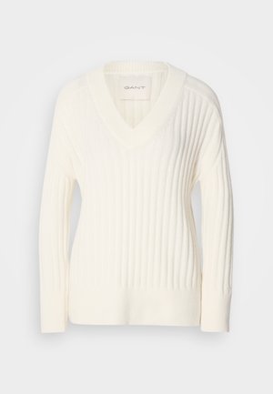 Krémový sveter s výstrihom do V a rebrovanou textúrou, dlhými rukávmi a voľným strihom. Obsahuje štítok s logom "GANT" blízko výstrihu.