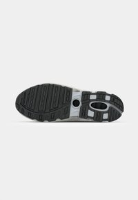Suela de zapatilla deportiva con un patrón de goma negra con ranuras y cortes, acentuada por una entresuela gris y elementos de diseño circulares.