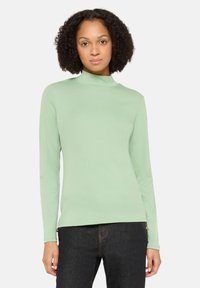 Hellgrüner Langarm-Turtleneck aus weichem Stoff, mit figurbetontem Schnitt und subtiler Textur, kombiniert mit dunklen Jeans.