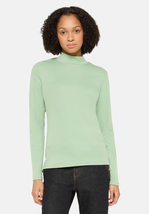 Hellgrüner Langarm-Turtleneck aus weichem Stoff, mit figurbetontem Schnitt und subtiler Textur, kombiniert mit dunklen Jeans.