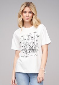 T-shirt en coton blanc à manches courtes, avec un design floral noir et le texte "wildflower club" en bas. Texture lisse.