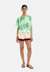 Koszulka z krótkim rękawem w zielony wzór palm, wykonana z lekkiego materiału; zestawiona z beżowymi szortami z bordowym akcentem u dołu. Klapki.