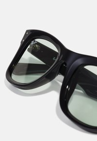 Ochelari de soare negri, supradimensionați, cu lentile verzi, având un cadru rotund și branding Ray-Ban pe lentile și pe brate. Finisaj neted.